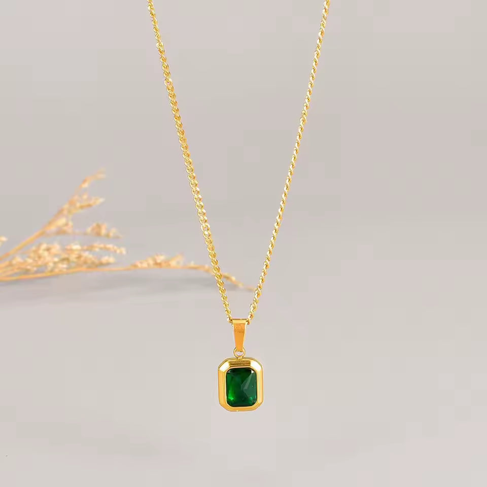Gold necklace with a green gemstone pendant on a light gray background