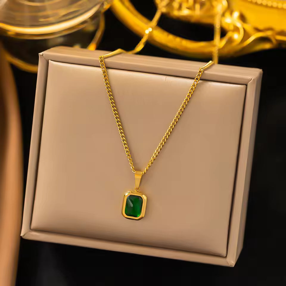 Gold necklace with a green pendant on a beige display box.