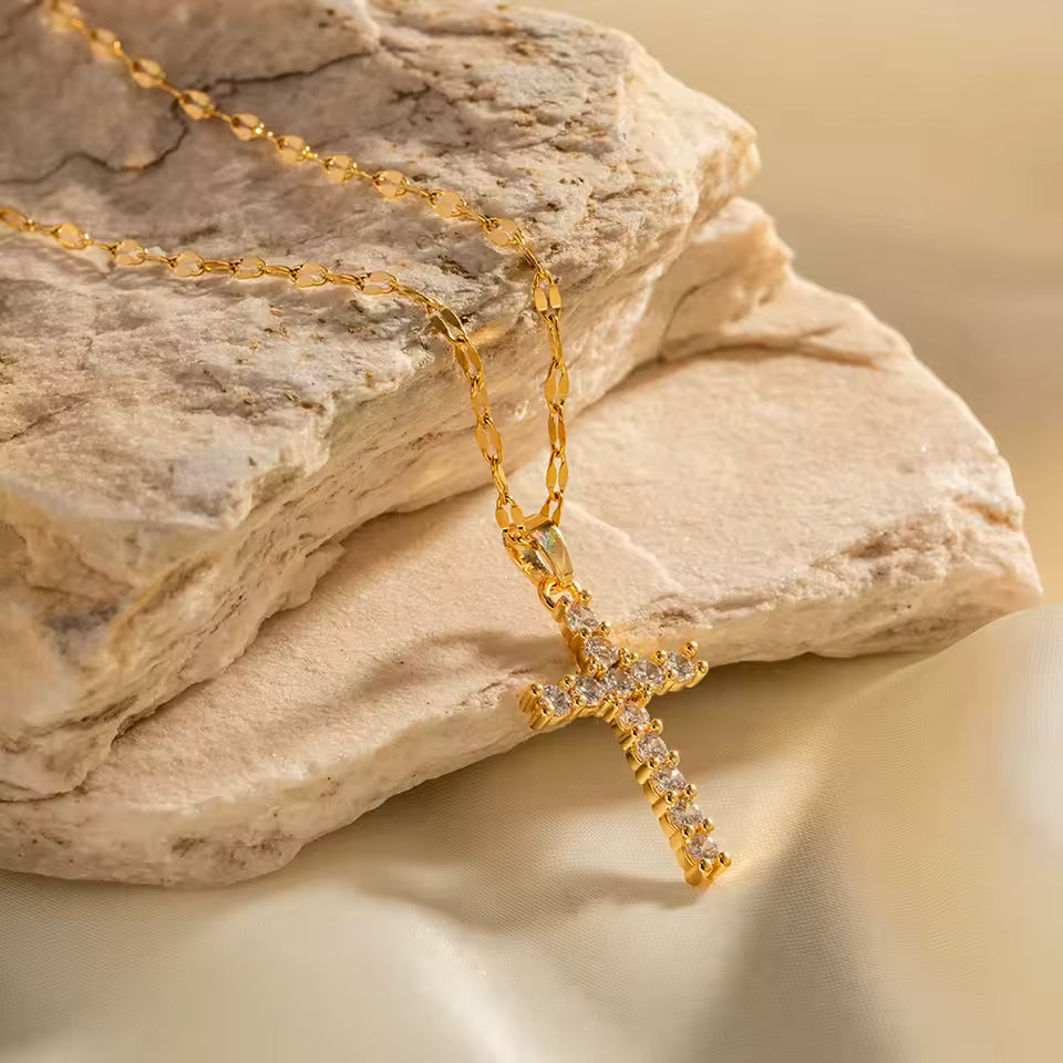 Gold necklace with a cross pendant on a stone surface