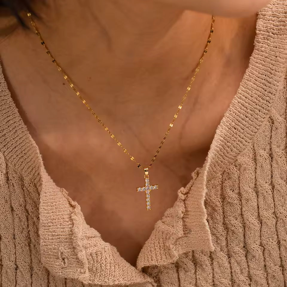Gold cross necklace on a person wearing a beige sweater