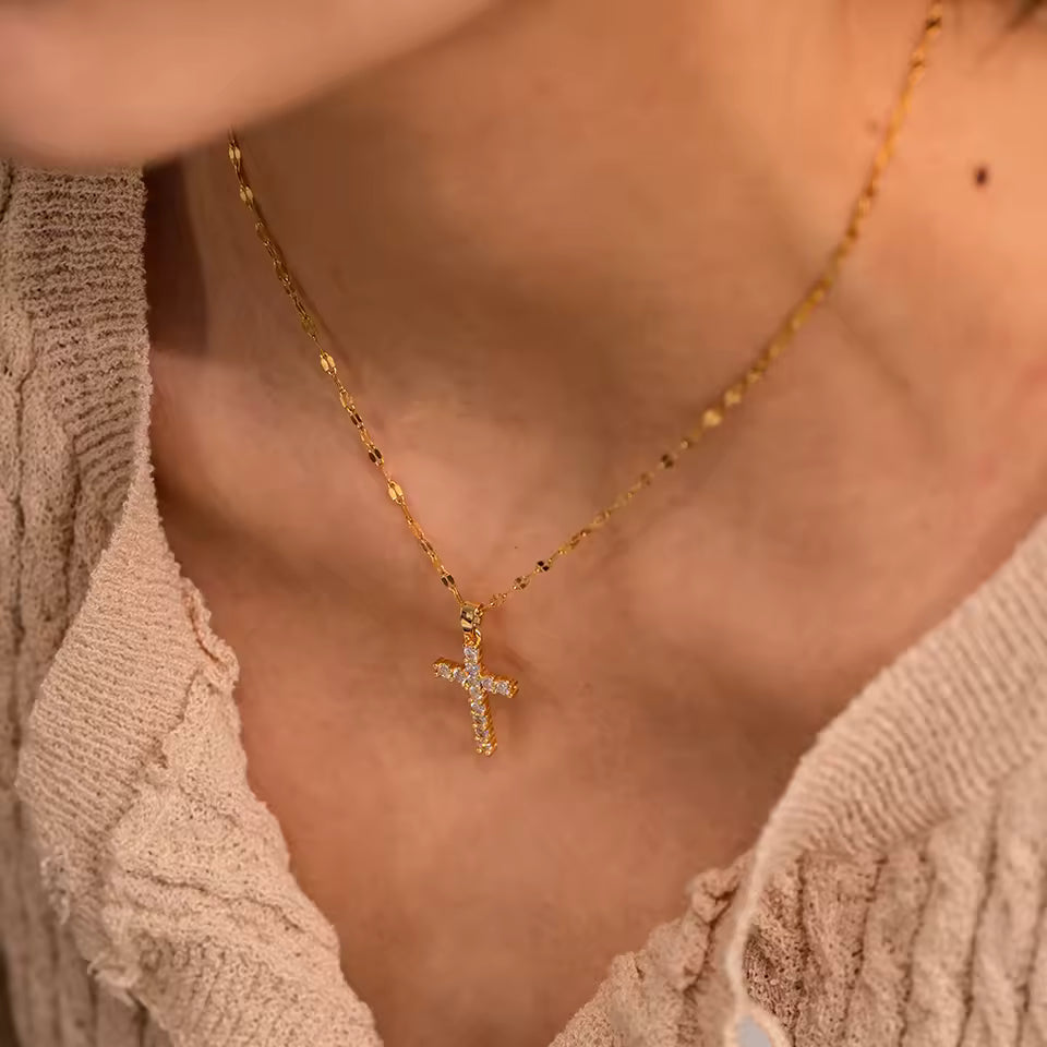 Gold necklace with a cross pendant worn by a person in a beige top.