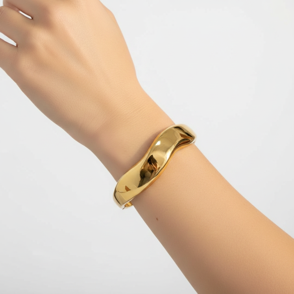 Gold cuff bracelet with wave design on woman's wrist with white background