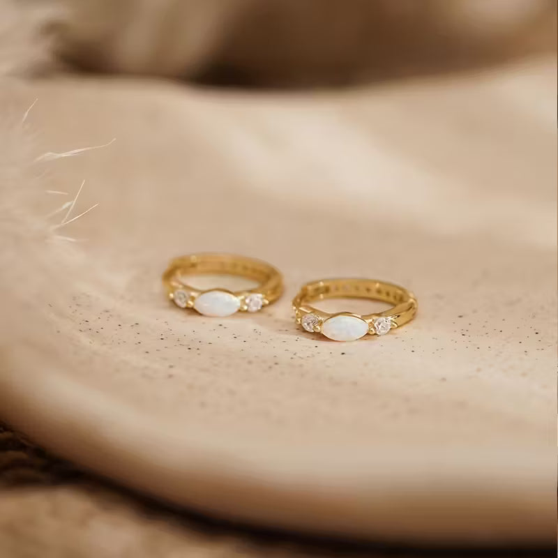 Two gold rings with gemstones on a beige surface
