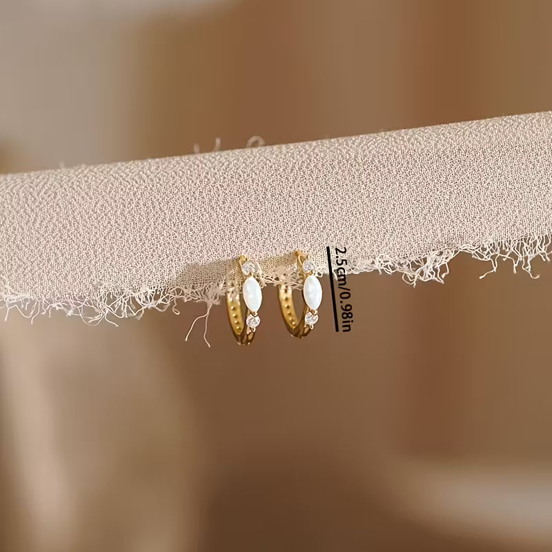 Gold hoop earrings on a textured beige surface with a blurred background