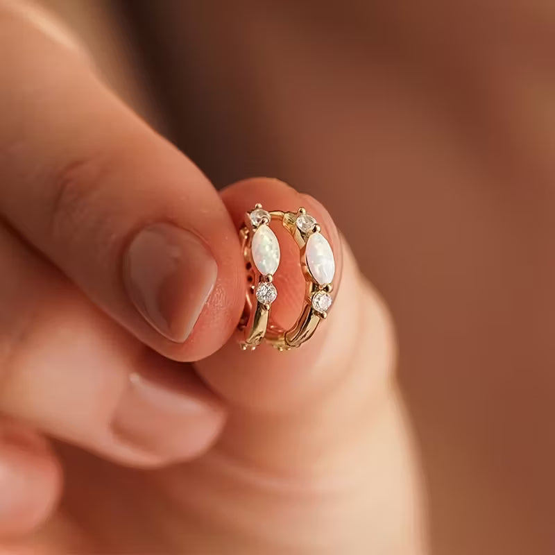 Gold hoop earrings with marquise-shaped stones held between fingers against a blurred background