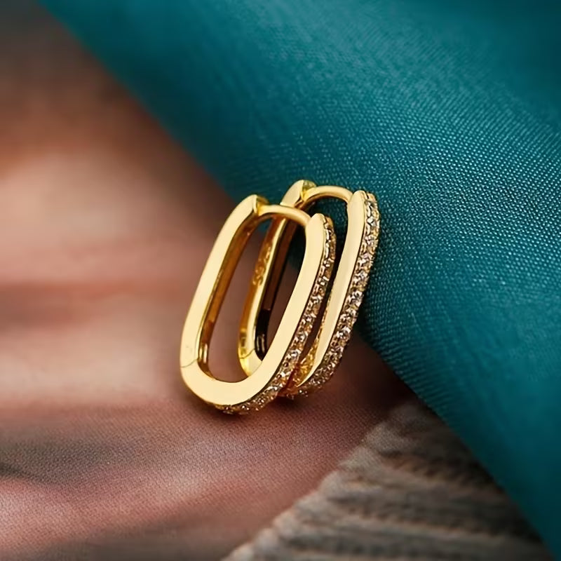 Gold hoop earrings on a person's ear against a teal fabric background