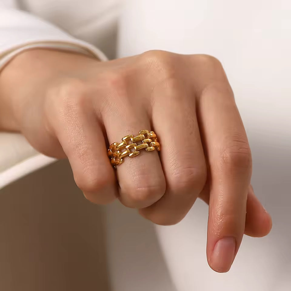 Gold chain ring on a person's finger with a neutral background
