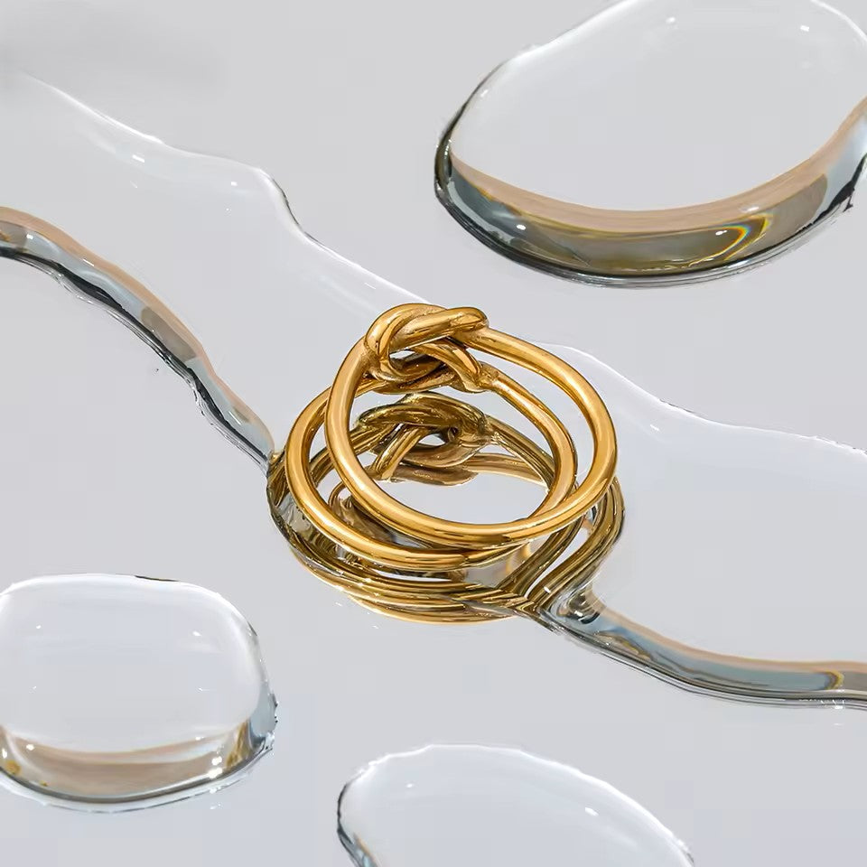Stack of gold rings on a white surface with a clear glass dish