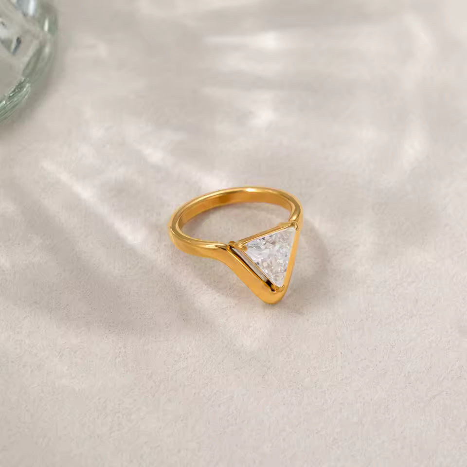 Gold ring with a triangular design on a light fabric background