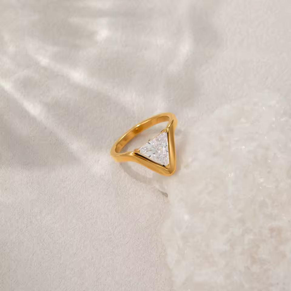 Gold triangle-shaped ring with a clear gemstone on a light beige fabric background