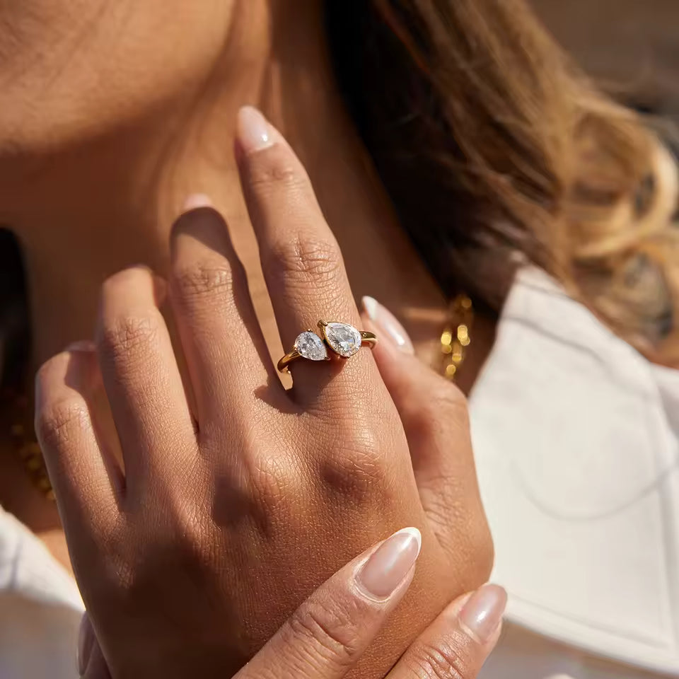 Close-up of a hand wearing a gold ring with two diamonds, blurred background