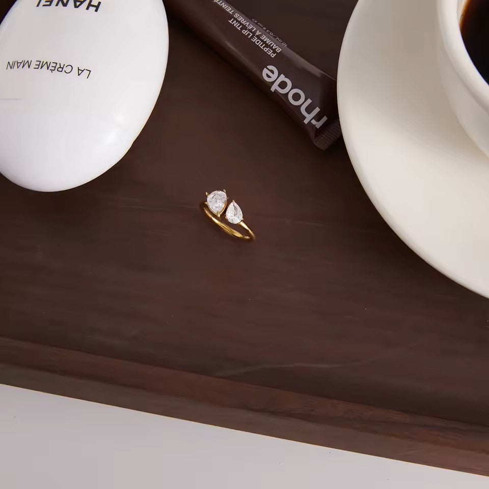 Gold ring with diamonds on a wooden surface next to a coffee cup and La Crème Man bottle.