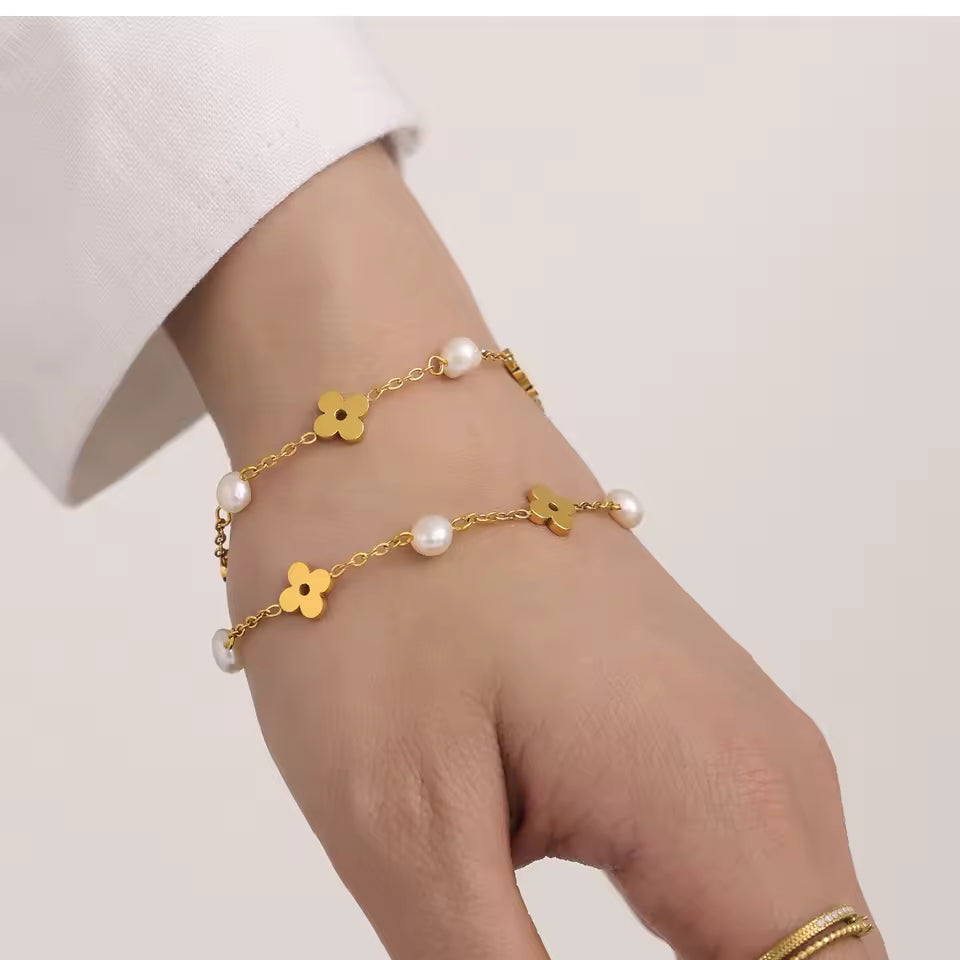 Gold bracelet with floral and pearl details on a wrist against a plain background