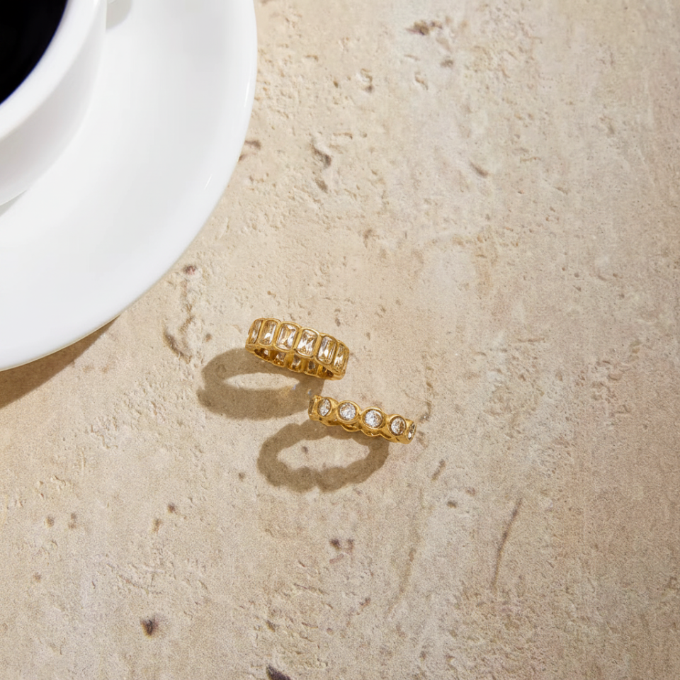 Gold rings on a textured beige surface with a white cup in the background