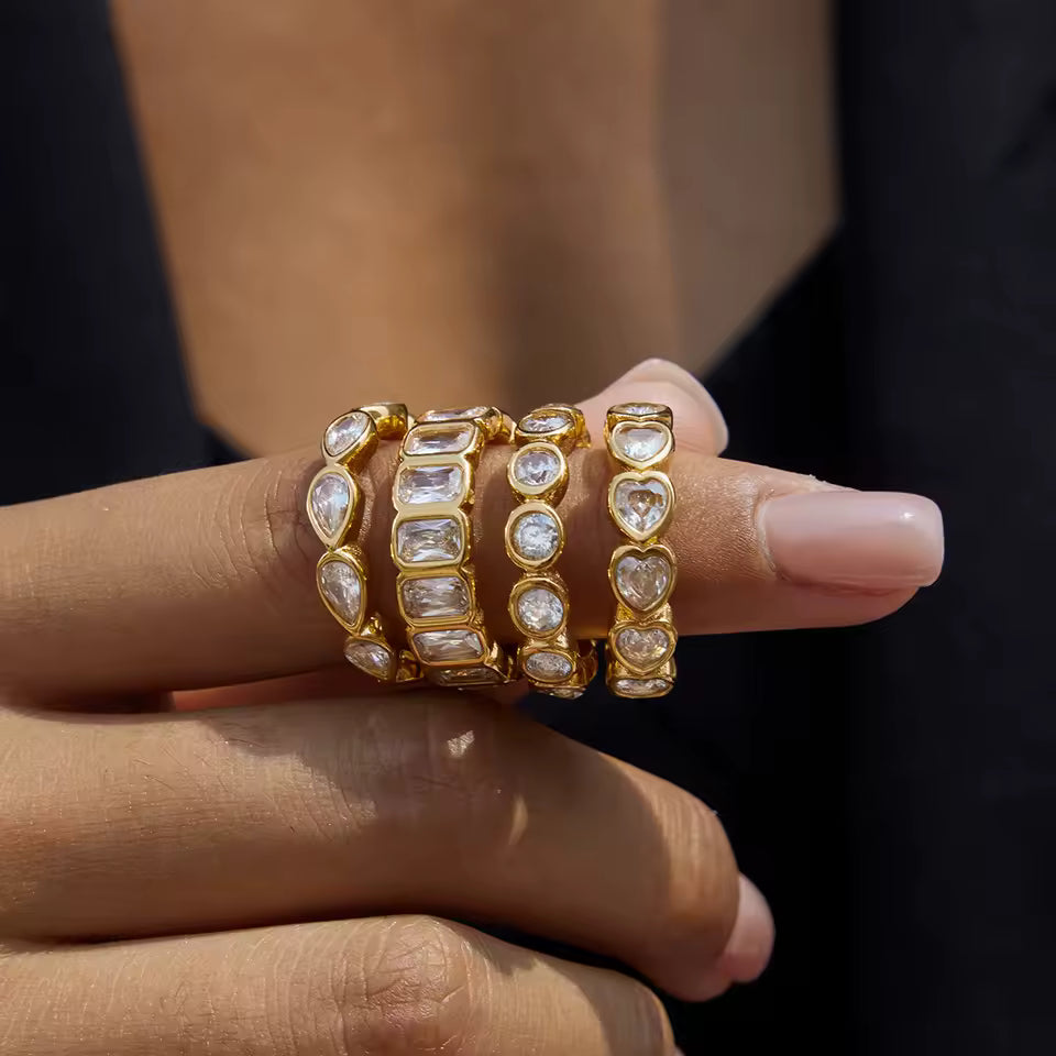 Gold rings with heart and square designs on a hand against a dark background