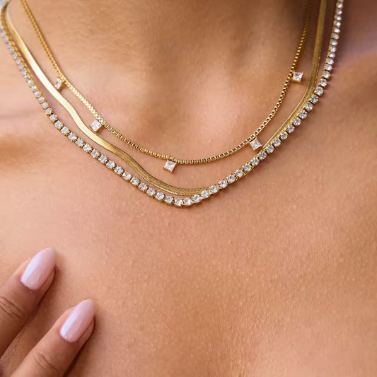 Close-up of a person wearing three gold necklaces with diamond accents on a light skin background.