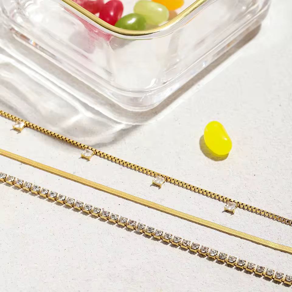Gold necklaces with small diamonds on a light surface with colorful candies in the background