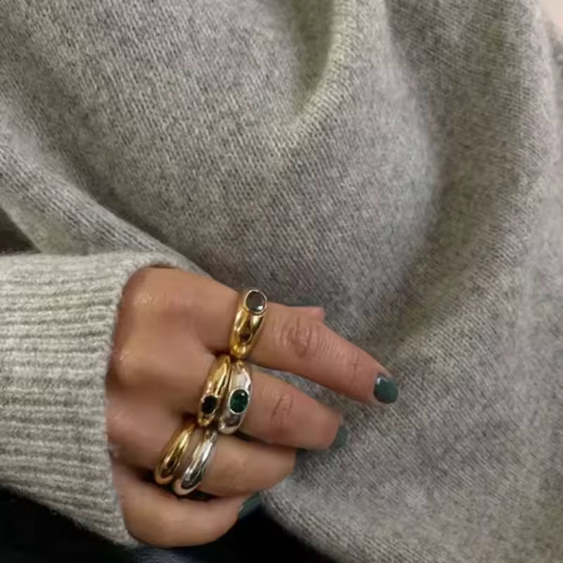 Hand wearing multiple rings with a gray sweater background