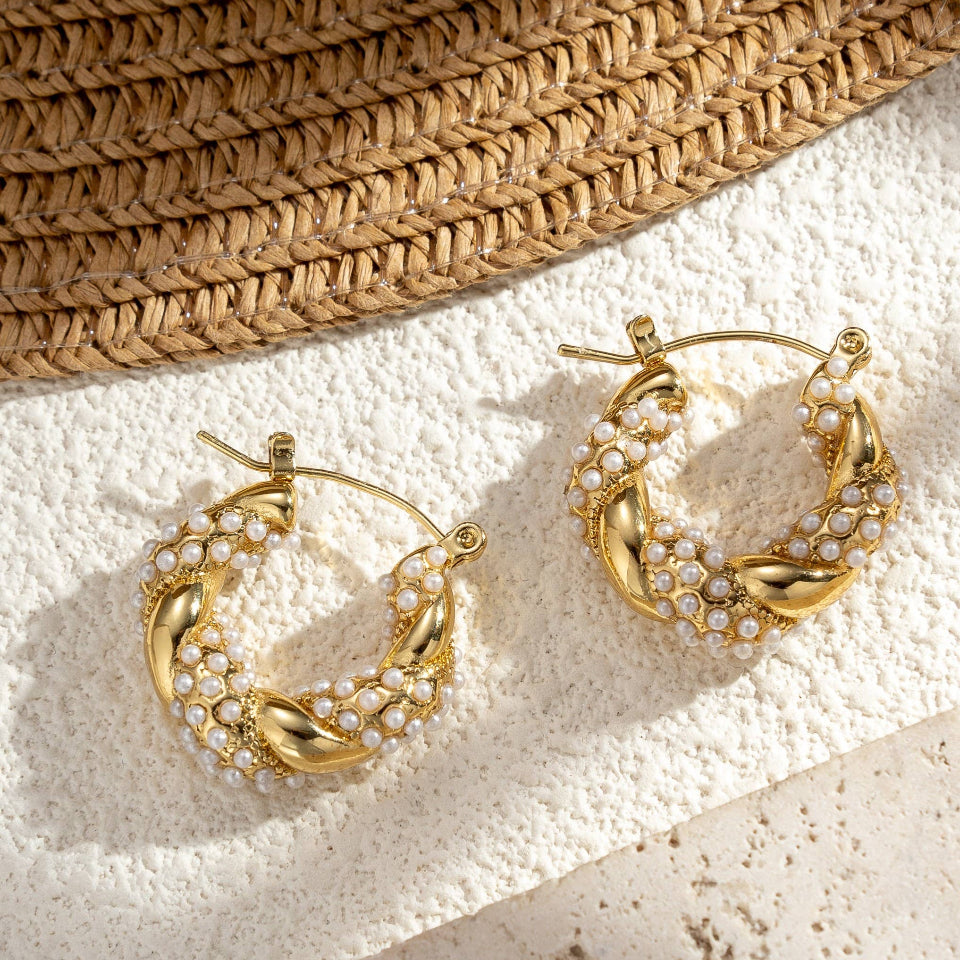 Gold hoop earrings with leaf-like designs on a textured surface with a straw hat in the background.