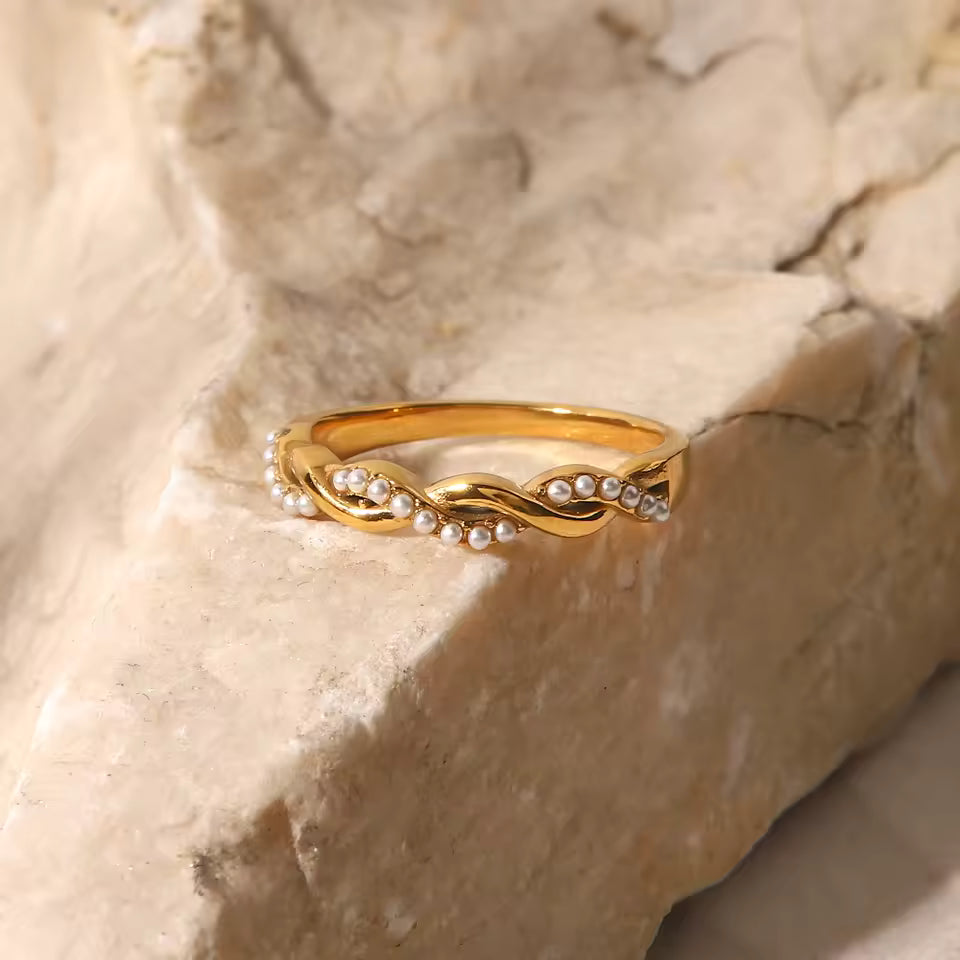 Gold ring with small pearls on a textured beige surface