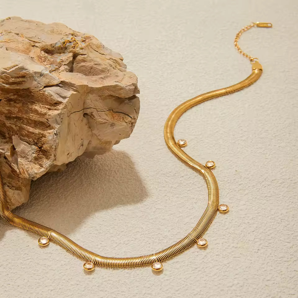 Gold necklace on a textured beige surface with a rock