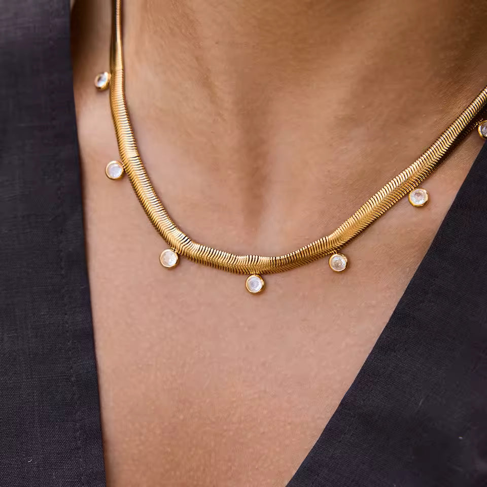 Gold necklace with small round pendants on a person wearing a black top.