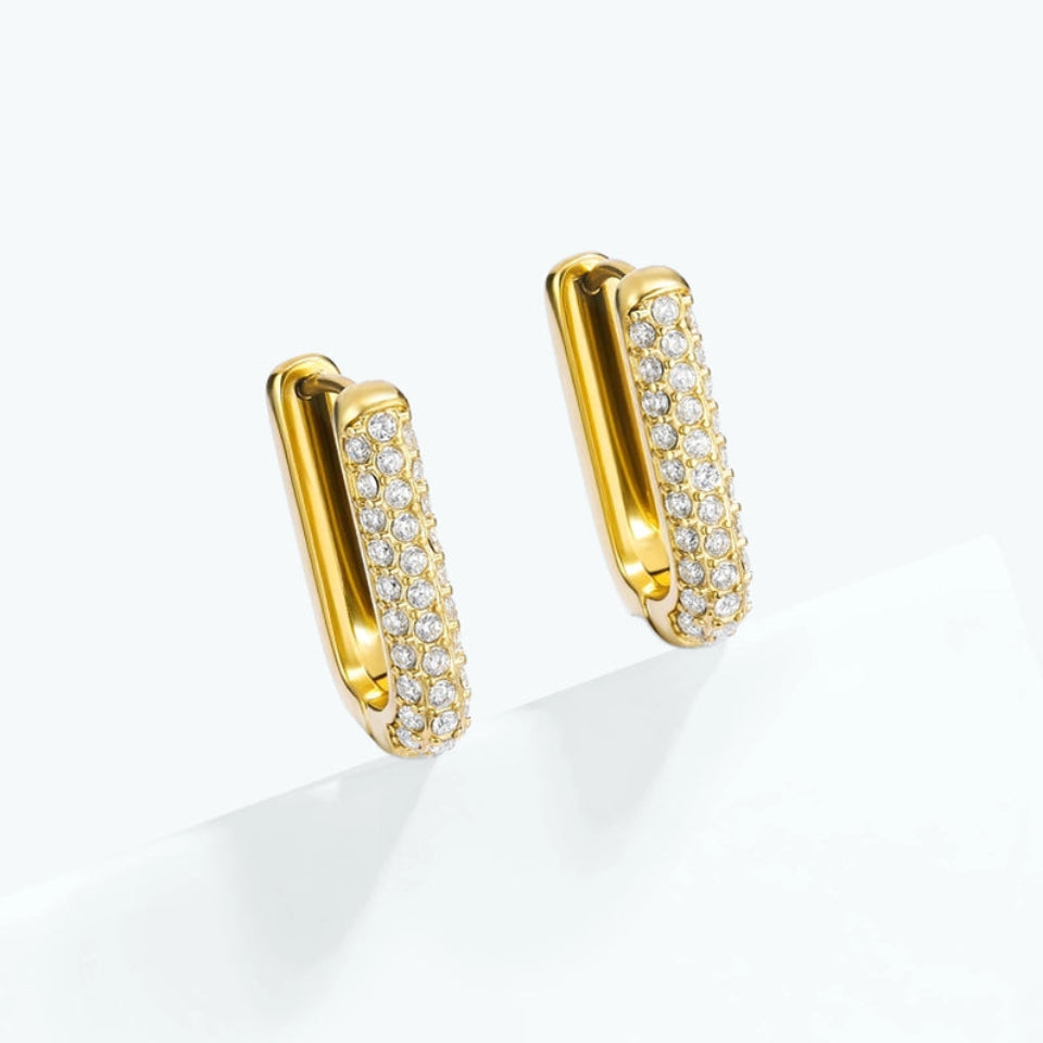 A pair of gold huggie hoop earrings paved with small clear stones, displayed on a clean white surface.