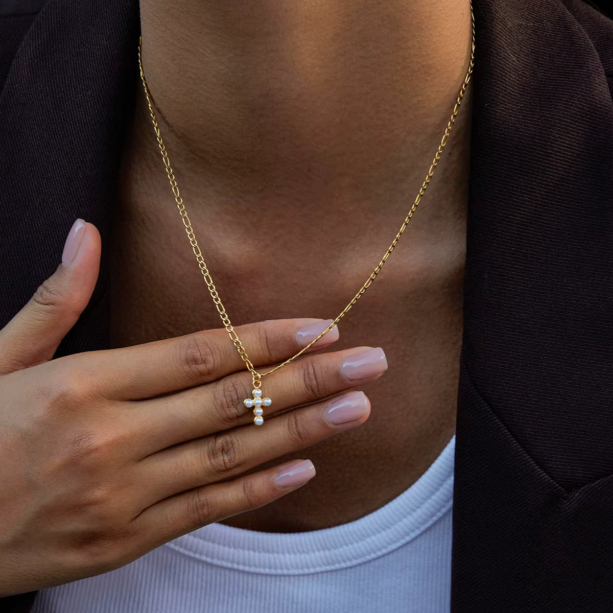 Gold necklace with a pendant worn by a person, with a hand touching the necklace.