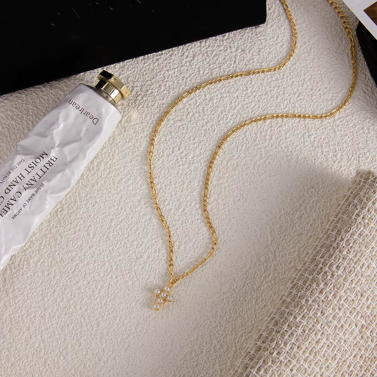 Gold necklace with a pendant on a textured surface next to a white tube.