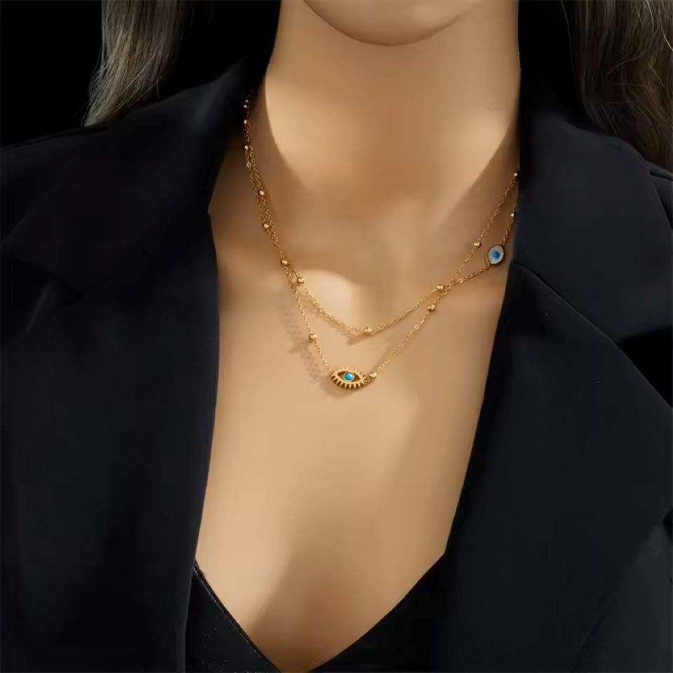 A close-up of a model wearing a double-layered gold necklace with evil eye charms, styled with a black blazer.