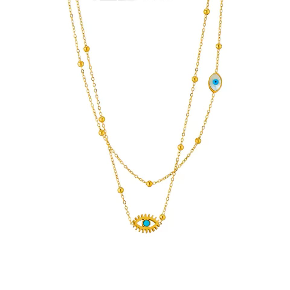 A double-layered gold necklace featuring a sunburst evil eye pendant with a turquoise blue center on the longer chain, and a matching evil eye charm on the shorter chain, set against a plain white background.