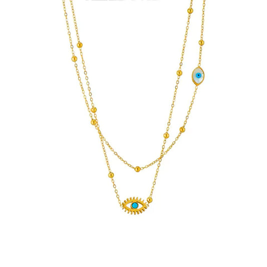 A double-layered gold necklace featuring a sunburst evil eye pendant with a turquoise blue center on the longer chain, and a matching evil eye charm on the shorter chain, set against a plain white background.