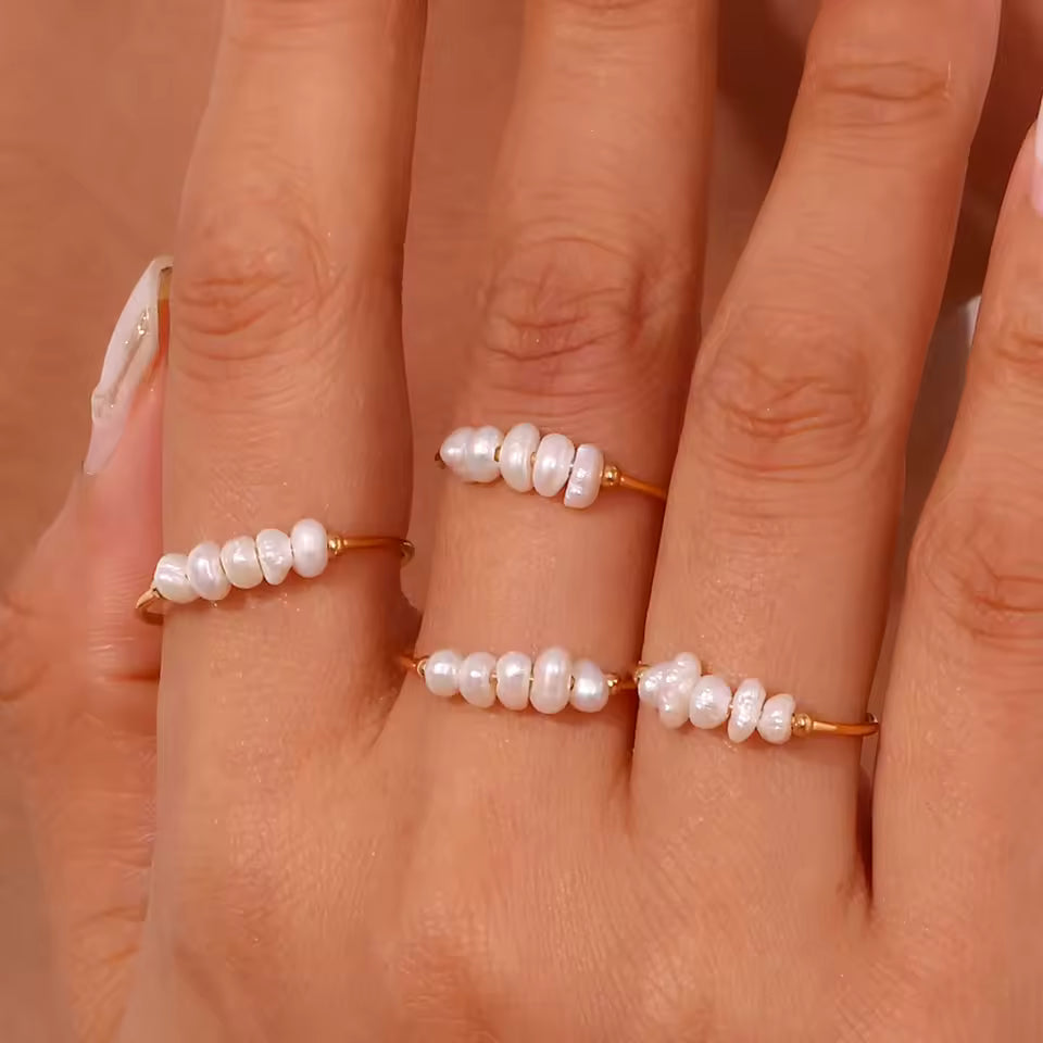 Close-up of a hand wearing three pearl rings on a neutral background