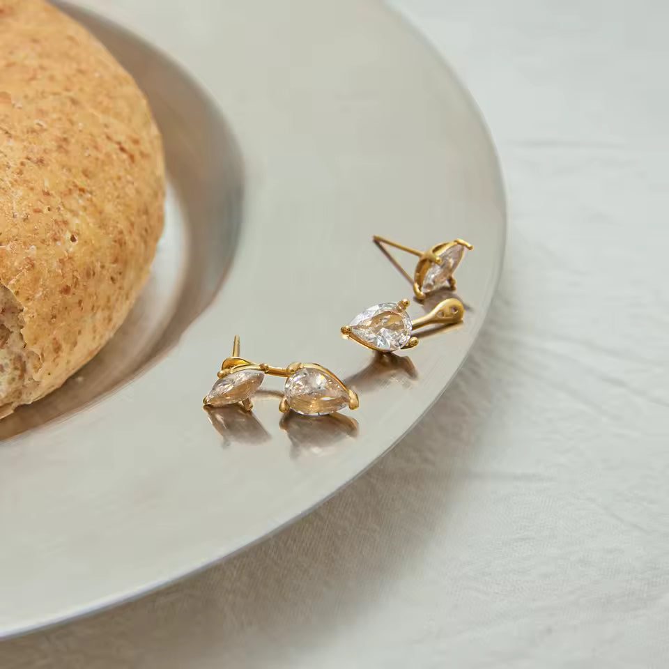 Gold earrings with clear stones on a white surface next to a loaf of bread