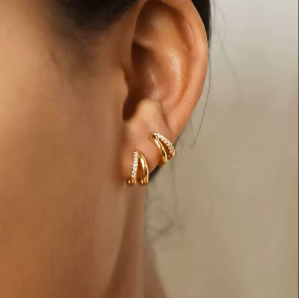 Close-up of an ear wearing gold hoop earrings with a neutral background