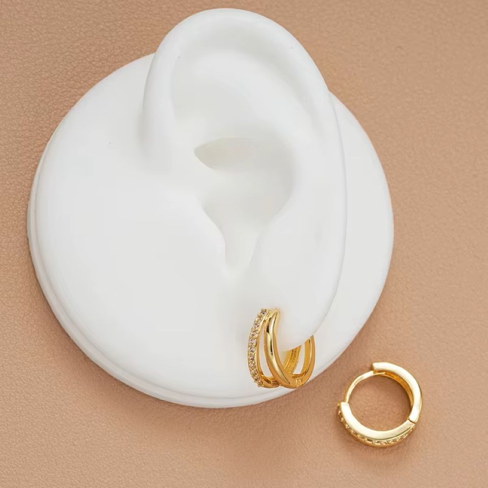 Gold hoop earrings on a white ear model with a beige background