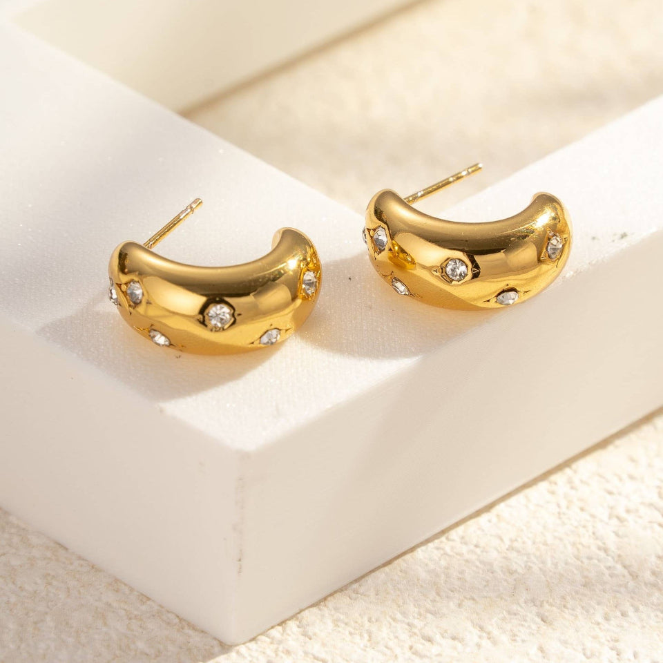 Gold hoop earrings with small stones on a light wooden surface