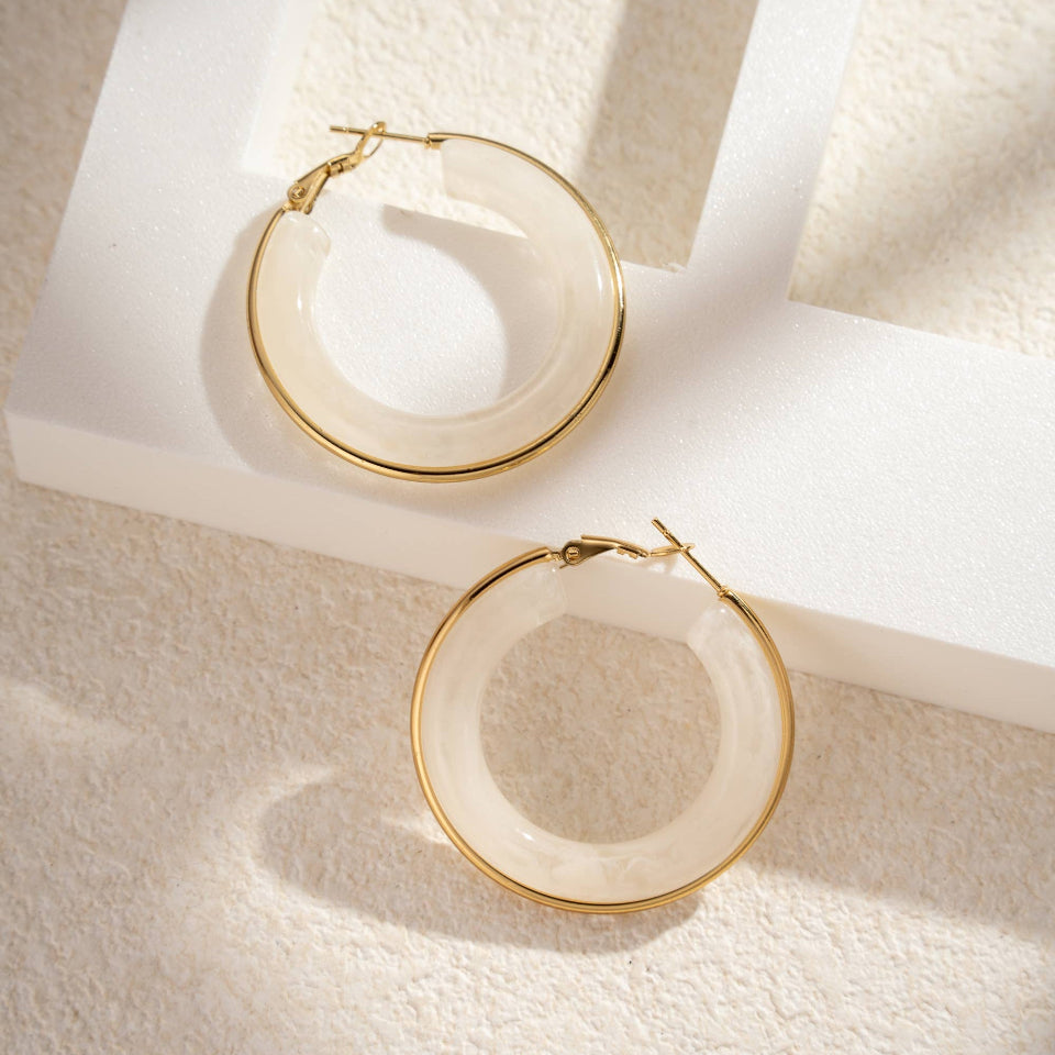 Gold hoop earrings on a textured white surface with soft shadows