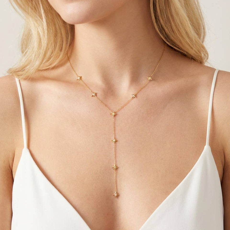 Woman wearing a gold necklace with a white top against a neutral background