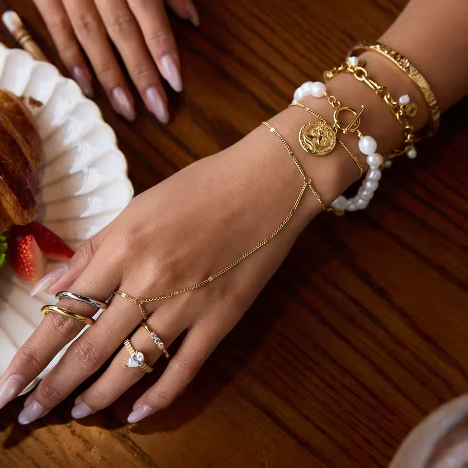 Close-up of a hand wearing multiple gold bracelets and rings on a wooden surface.