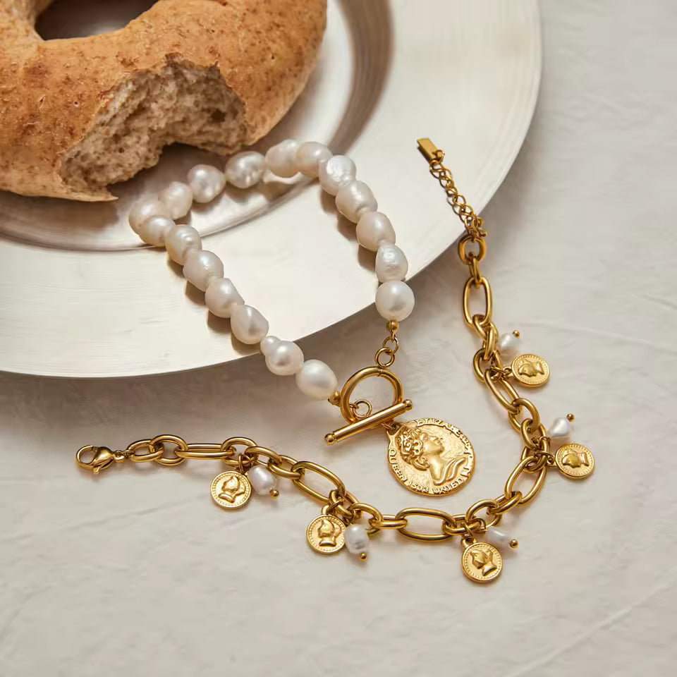 Gold bracelet with charms and pearl necklace on a plate with bread
