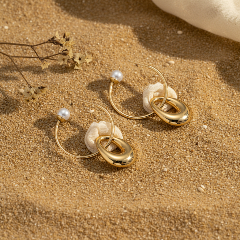 Gold hoop earrings with pearls on a sandy surface